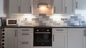 A modern kitchen with white cabinets, a Bosch oven, a microwave, and a glass-fronted range hood. - Charming cottage in a great location in Dover, just 10 minutes walk from the beach (Dover)
