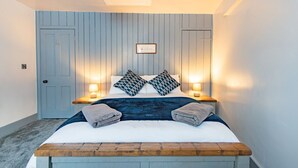 A bedroom with a bed, bedside lamps, a wooden bench, and a door. - Charming cottage in a great location in Dover, just 10 minutes walk from the beach (Dover)