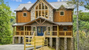 A two-story log cabin with a stone foundation, wooden exterior, and a blue front door. - Stargazer Chalet 5 Bedroom Cabin by RedAwning (Sevierville)