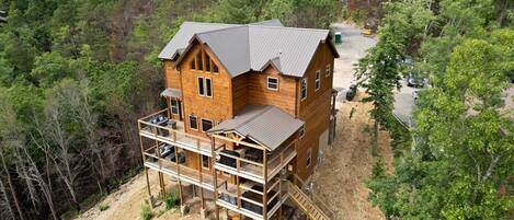 A wooden cabin with a balcony and a staircase leading to a deck, surrounded by dense forest.