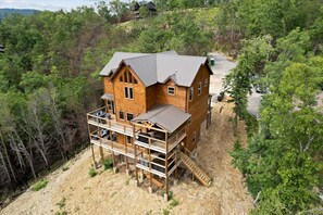 Eine Holzhütte mit Balkon und einer Treppe zu einer Terrasse, umgeben von dichtem Wald.