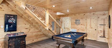Un intérieur en bois avec une table de billard, un escalier et un juke-box.