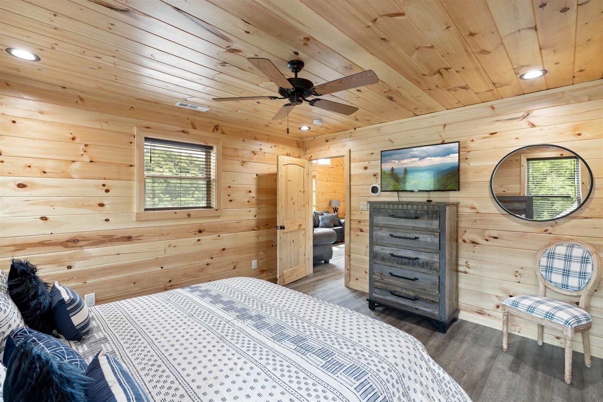 A wooden-paneled bedroom with a bed, dresser, chair, ceiling fan, and a painting on the wall.