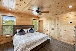 Ein Schlafzimmer mit Holzwandverkleidung, einem Bett, einem Deckenventilator und einem Fenster mit Jalousien.