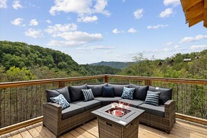 Eine Terrasse mit einer gebogenen Couch und einem Feuerkorb, mit Blick auf eine bewaldete Landschaft.