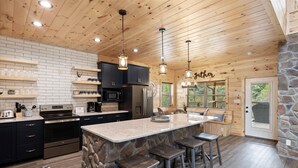A modern kitchen with a stone island, bar stools, and pendant lighting. - Stargazer Chalet 5 Bedroom Cabin by RedAwning (Sevierville)