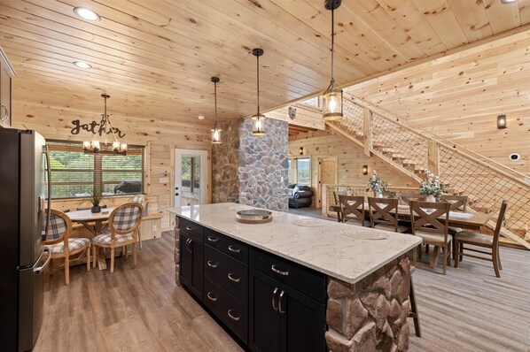A wooden cabin interior with a kitchen, dining area, and a stone accent wall.