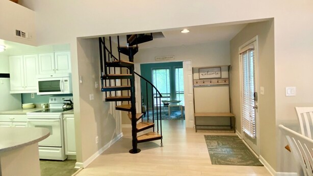 A spacious kitchen with white cabinets and a built-in oven, a black spiral staircase, and a view of the living area.