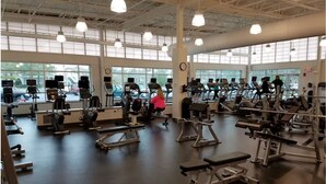 A gym with exercise equipment, large windows, and a high ceiling.