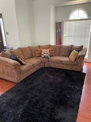 A living room with a sectional sofa, a black furry rug, and a dining table with chairs.
