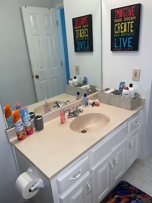 A bathroom with a sink, mirror, and various toiletries. There are motivational posters on the wall and a basket of personal items.