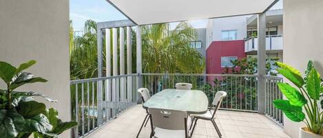 A balcony with a table and chairs, surrounded by potted plants and a view of buildings and greenery.
