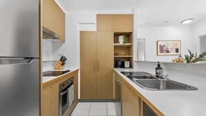 A modern kitchen with stainless steel appliances, wooden cabinets, and a white countertop. - Home away from Home! 2Bed/1Bath/Car/Pool~2kms CBD (Fortitude Valley)