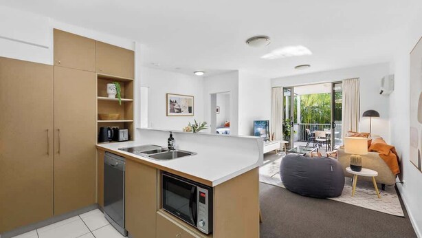 A compact kitchen with a built-in microwave, a sink, and a dishwasher. There is a seating area with a sofa and a lamp. - Home away from Home! 2Bed/1Bath/Car/Pool~2kms CBD (Fortitude Valley)