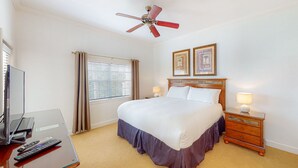 A hotel room with a bed, bedside table, lamp, ceiling fan, window with curtains, and a TV on a stand. - Cozy Condo with Third Floor Balcony at Reunion (Kissimmee)