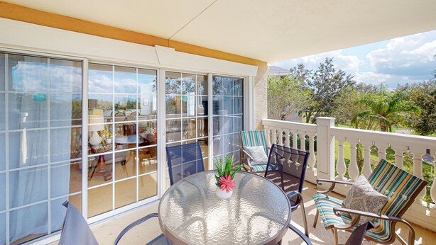 A balcony with a glass door, a round table with a vase, and striped chairs. - Cozy Condo with Third Floor Balcony at Reunion (Kissimmee)