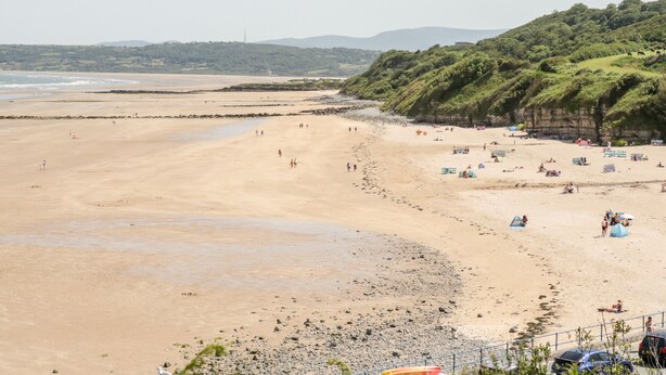 A beach with a rocky shoreline, umbrellas, and people. - Gwel Y Môr (Beaumaris)
