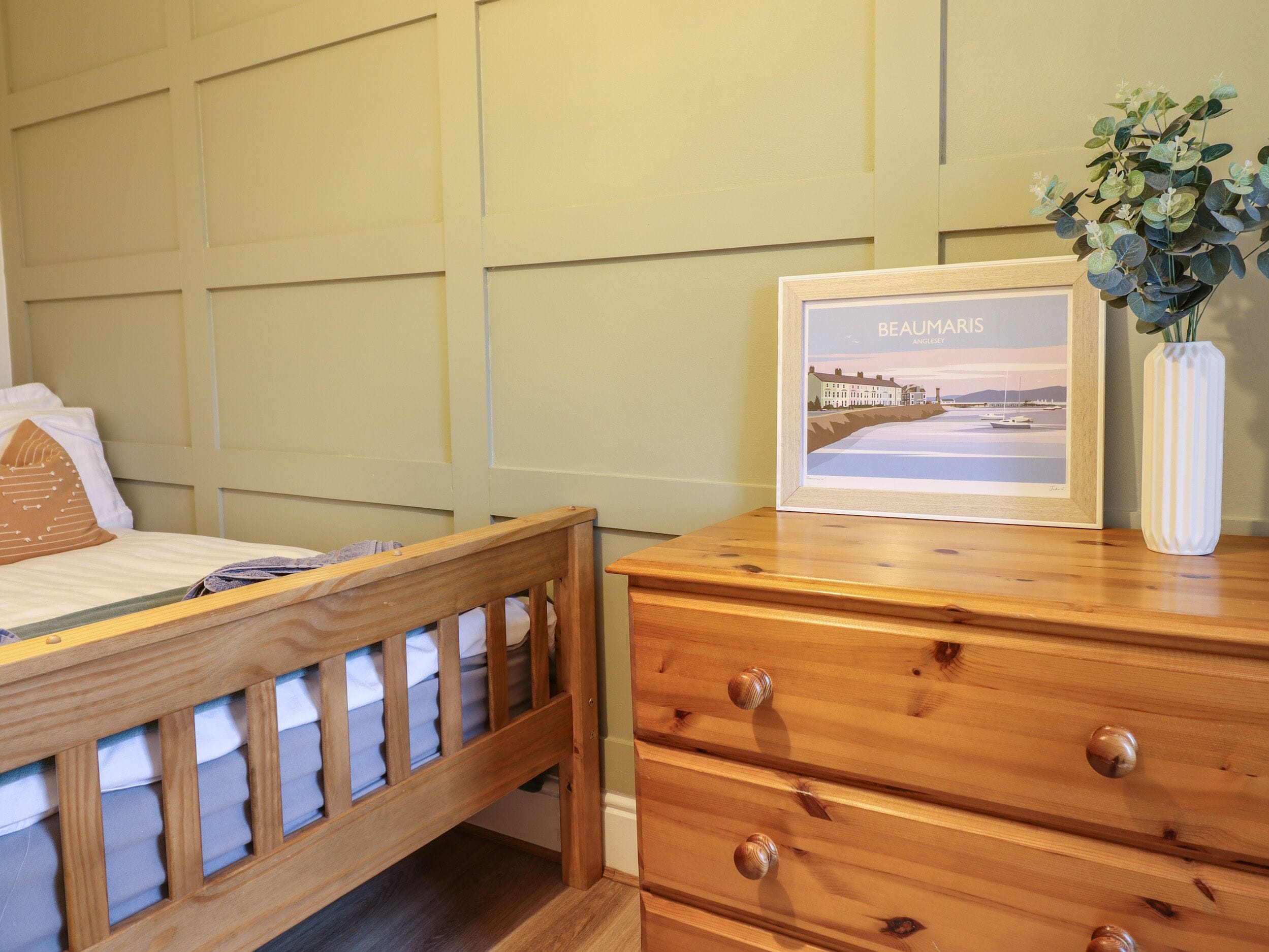 A bedroom with a wooden bed, a nightstand, a dresser, and a framed picture of a cityscape.