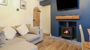 A living room with a sofa, a fireplace, a television, and a door. - Gwel Y Môr (Beaumaris)