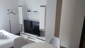 Ein modernes Hotelzimmer mit einem Bett, einem runden Tisch mit Stühlen, einem Fernseher und einem Kleiderschrank.