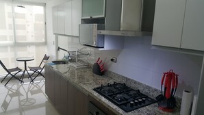 A modern kitchen with a gas stove, a sink, and a small dining area with chairs and a table. - Miraflores Upper Pardo Apartment 3bedroom/4baths (Miraflores)