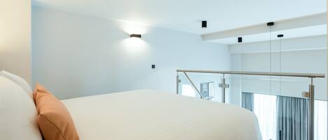 Una habitación de hotel moderna con una cama grande, un balcón con barandilla de vidrio y vista a la ciudad.