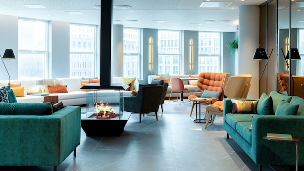 Un salon moderne doté d’une cheminée, de sièges confortables et de grandes fenêtres offrant une vue sur la ville.