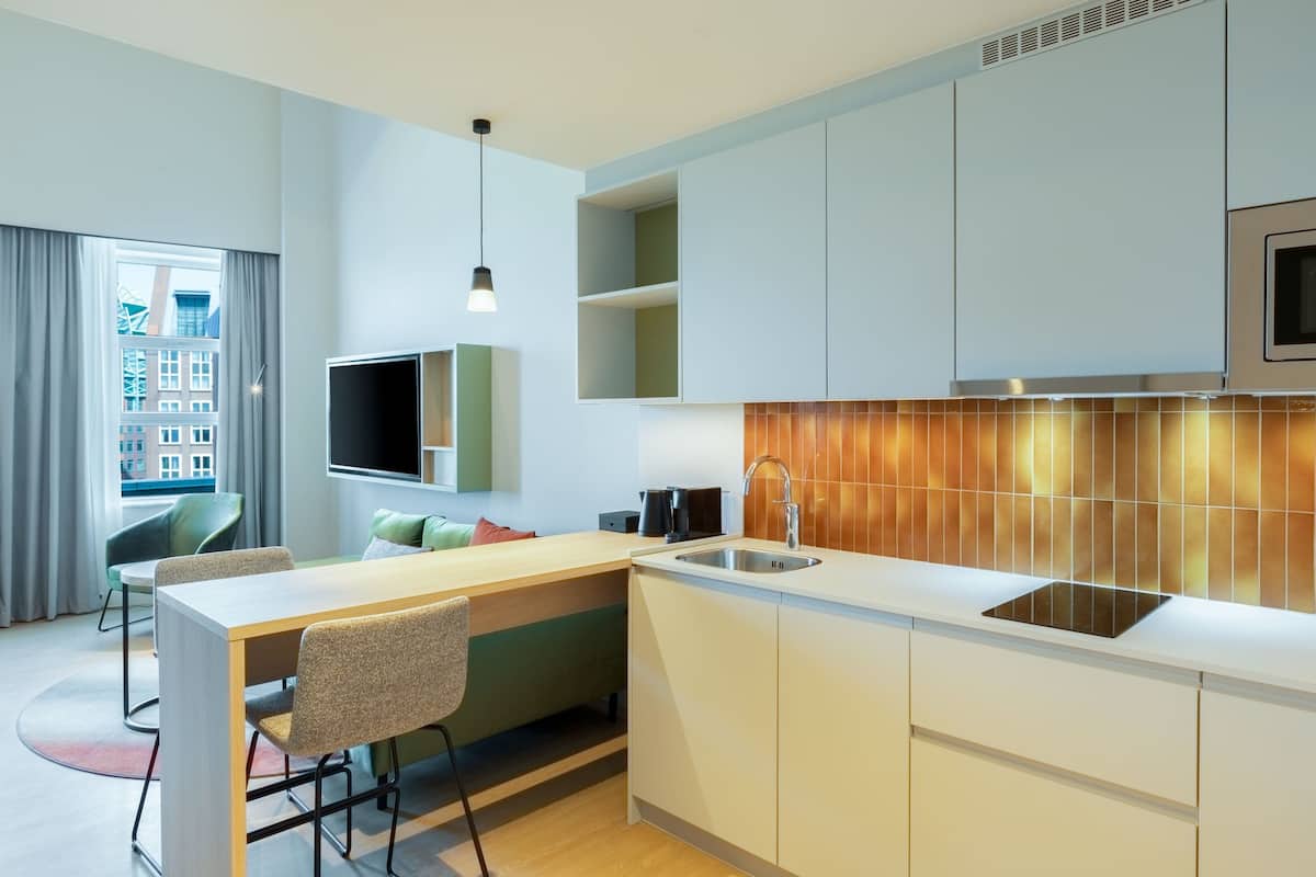 A modern kitchen with a built-in island, a flat-screen TV, and a large window with curtains.