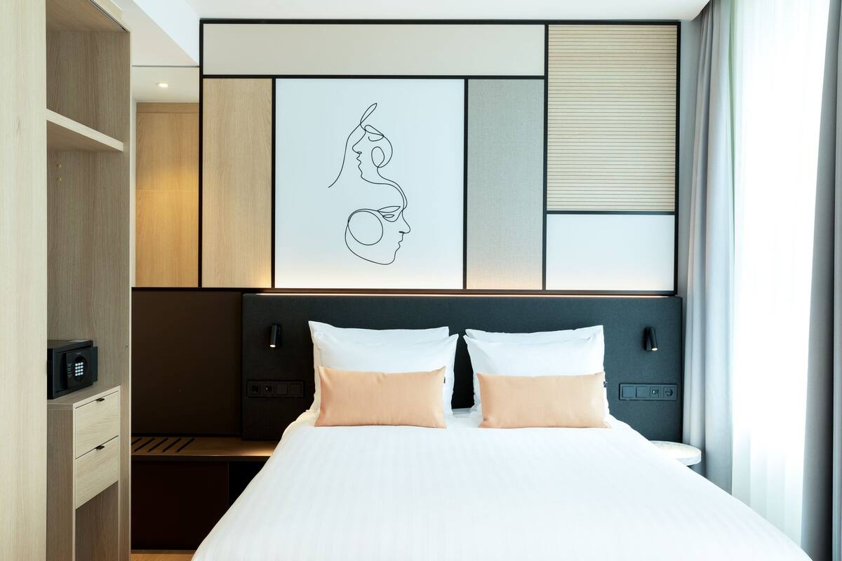 A modern hotel room with a large bed, a headboard with a geometric design, a microwave, and a bedside table.