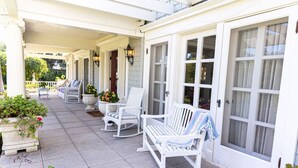 A covered porch with white rocking chairs and a bench, potted plants, and a white door with glass panels. - Beautiful Family Home near Rose Bowl, Dodger Stadium & Downtown Los Angeles. (Pasadena)