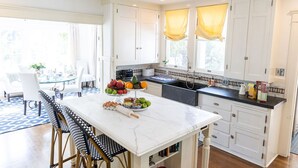 A modern kitchen with white cabinets, a marble countertop, and a dining area with a glass table and chairs. - Beautiful Family Home near Rose Bowl, Dodger Stadium & Downtown Los Angeles. (Pasadena)