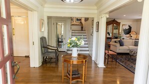 A spacious living room with a wooden floor, a white vase with flowers, a sofa, and a staircase in the background. - Beautiful Family Home near Rose Bowl, Dodger Stadium & Downtown Los Angeles. (Pasadena)