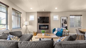 A modern living room with a fireplace, a flat-screen TV, and a dining area with a table and chairs. - Exceptional Location & Vibes, New Décor, Artwork, & Furnishing, Community Pool, 8 Miles to Portland (Beaverton)
