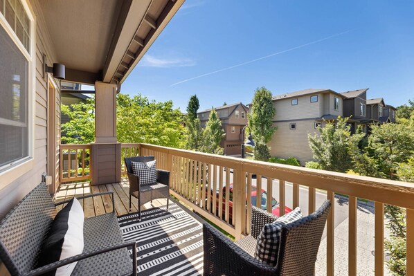 A balcony with outdoor furniture, a view of neighboring buildings, and a clear sky.