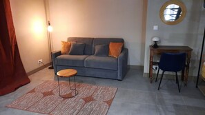 A living room with a grey sofa, a small wooden side table, a blue chair, a patterned rug, and a floor lamp.