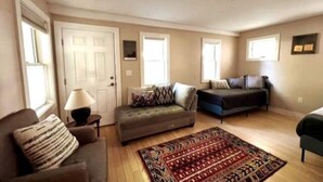 Un salon comprenant un canapé, une causeuse, un tapis à motifs et une lampe.
