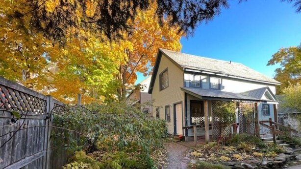 Une maison à deux étages avec un porche, une clôture en bois et un chemin menant à l’entrée.