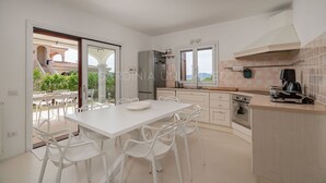 A modern kitchen with white cabinetry, a large island, and a view of the outdoors. - Villa Càrula: Private swimming pool near Lu Impostu (San Teodoro)
