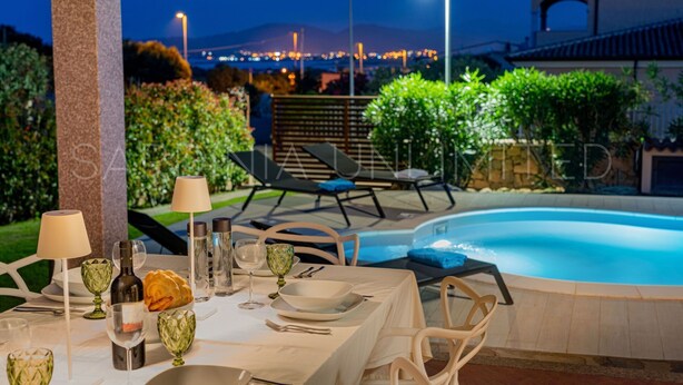 A dining area with a poolside setting, featuring a table set for two with glasses, plates, and a bottle. - Villa Càrula: Private swimming pool near Lu Impostu (San Teodoro)