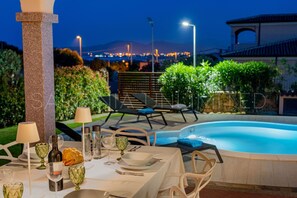 Un área de comedor con ambiente de piscina, con una mesa para dos, copas, platos y una botella.
