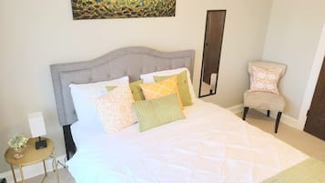 A neatly made bed with a quilted white duvet and several patterned pillows.