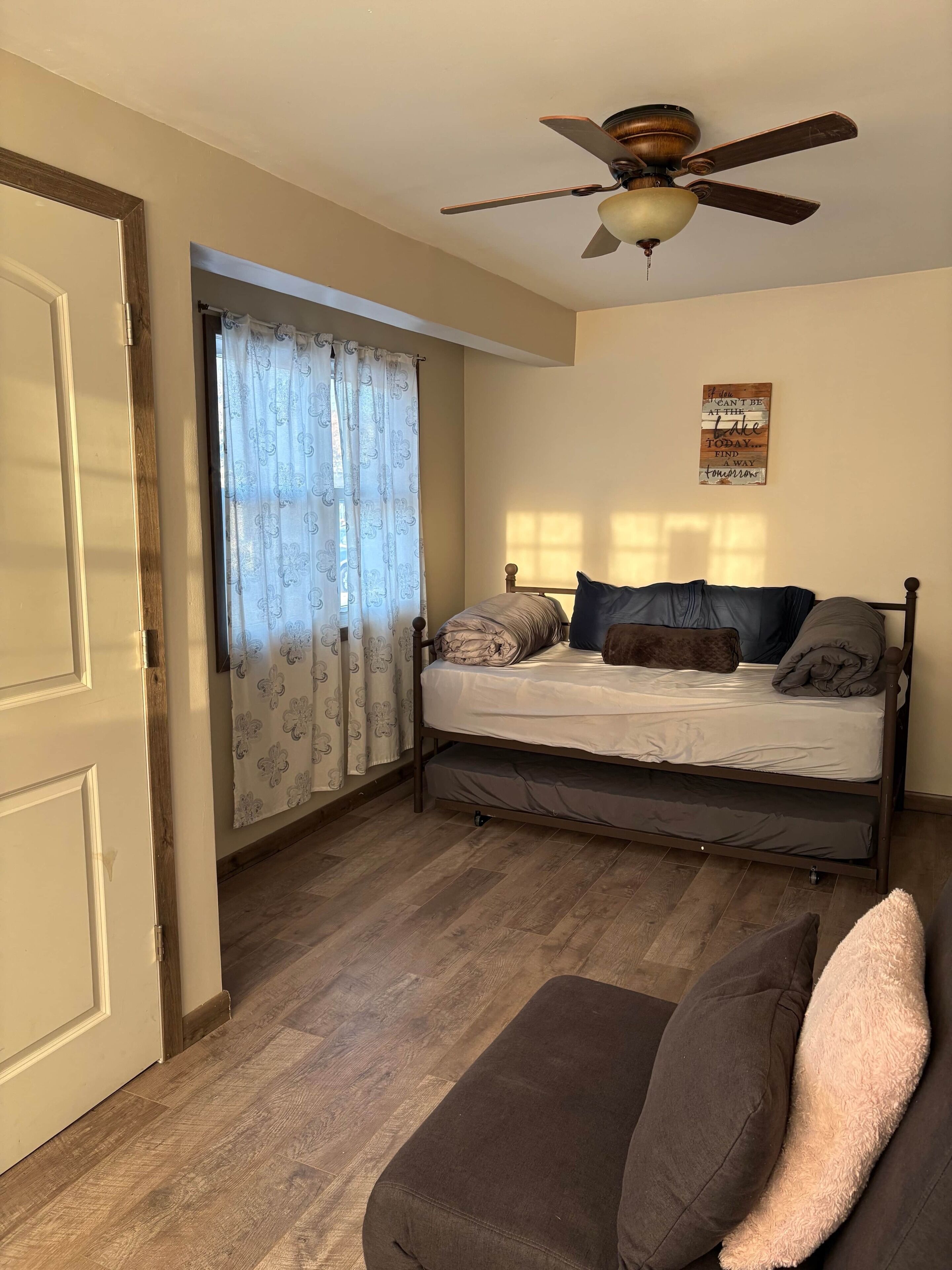 A bedroom with a bed, a ceiling fan, and a motivational quote on the wall.