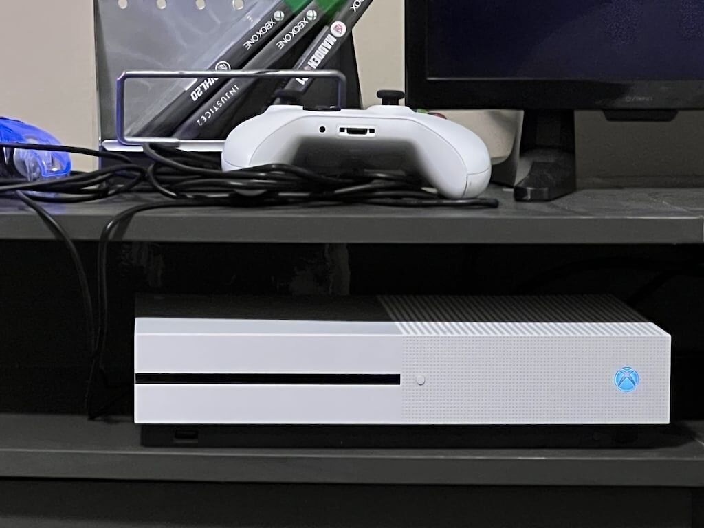 Une console Xbox blanche posée sur une surface noire, avec un écran et une manette Xbox verte.