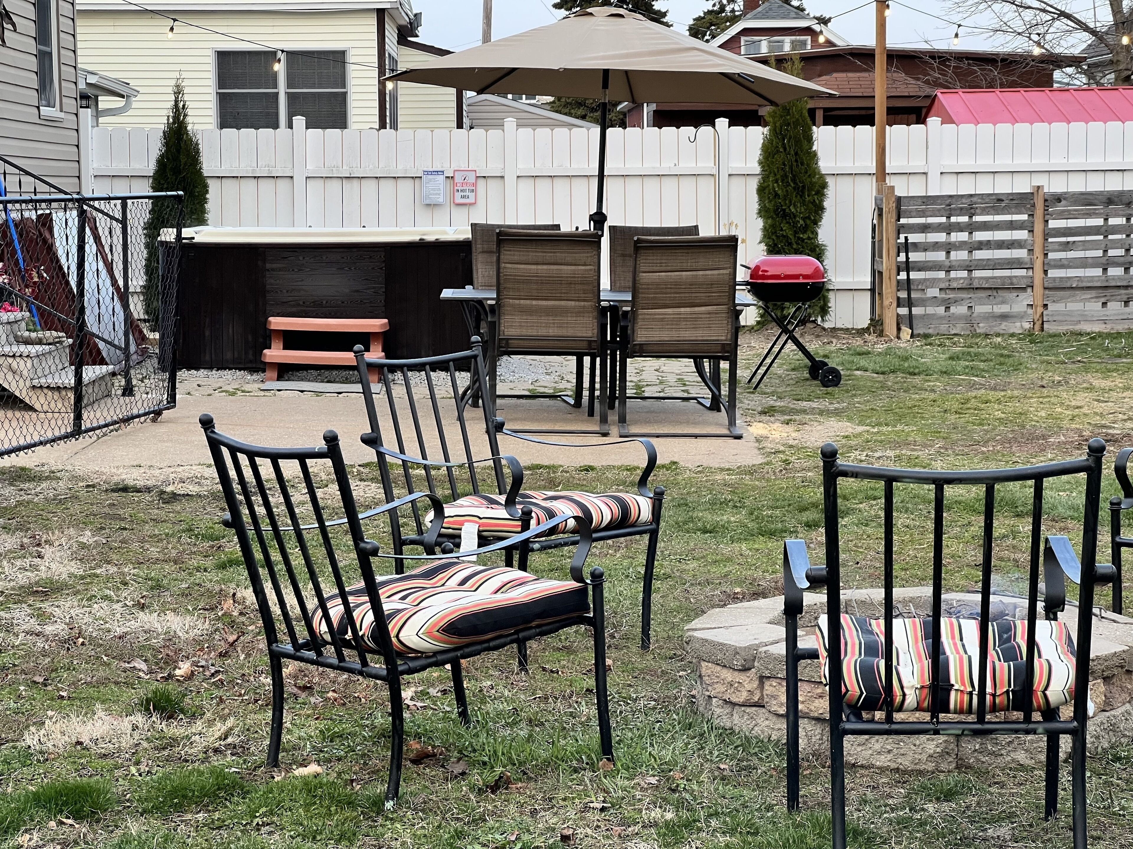 Een achtertuin met een barbecueplek, buitenzitplaatsen en een omheind gazon.