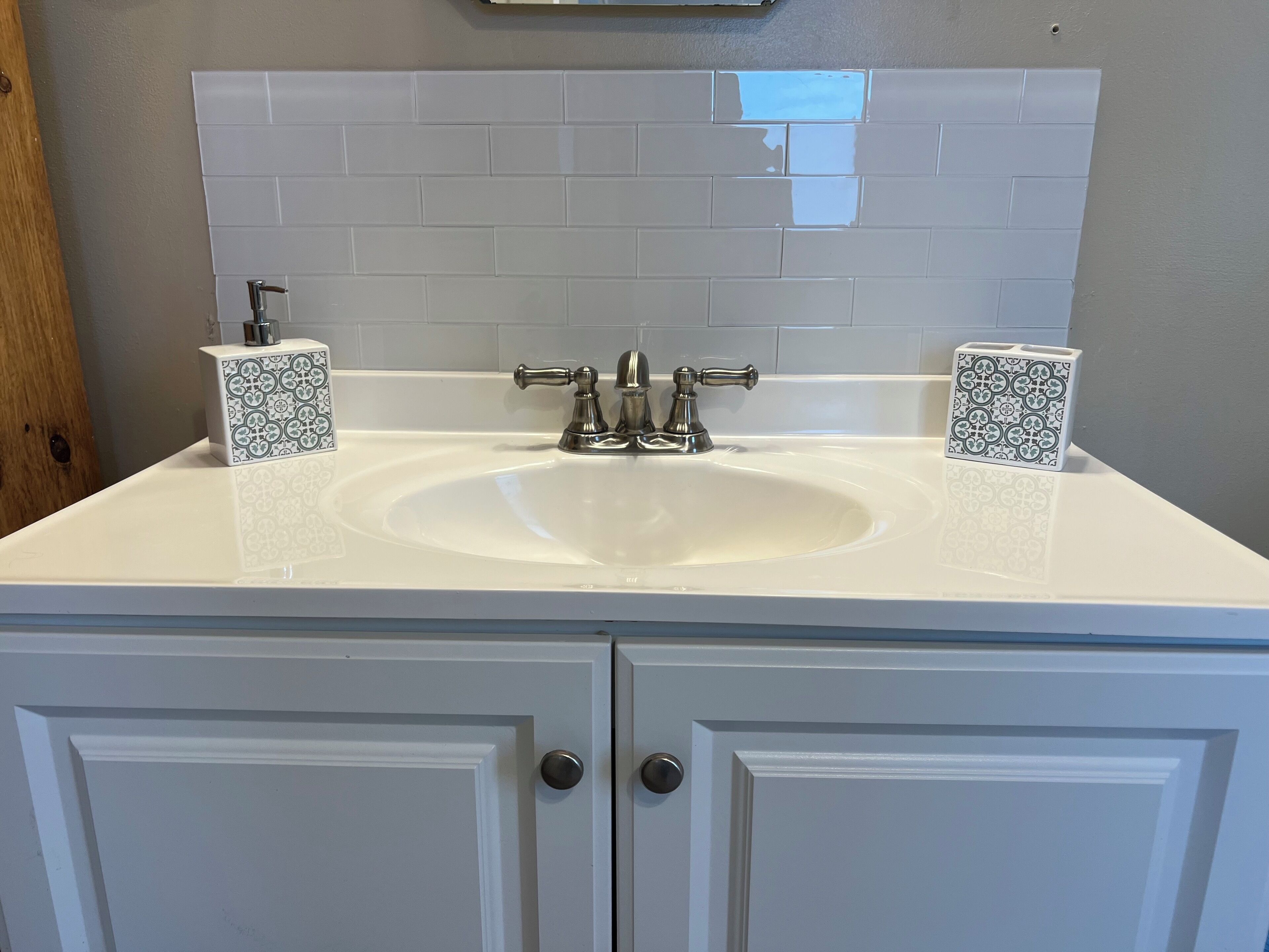 A bathroom with a white sink, two patterned soap dispensers, and a tiled backsplash.