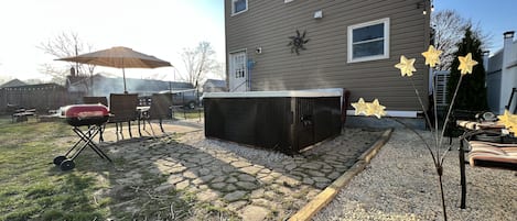 A backyard with a hot tub, patio furniture, and a house in the background.