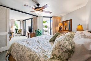 Ein Hotelzimmer mit einem großen Bett, einem Deckenventilator, einem Fernseher, einem Balkon mit Vorhängen und Blick ins Freie.