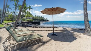 Ein Strand mit Liegestühlen und einem Sonnenschirm, Palmen und Blick aufs Meer.