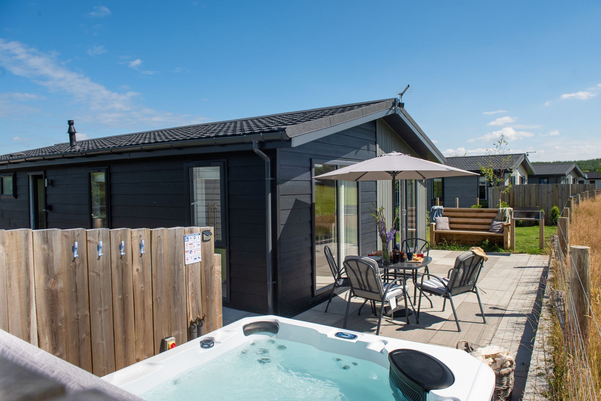 Ein modernes Haus mit einer Terrassenanlage, die ein Whirlpool, Sitzgelegenheiten im Freien und ein Holzzaun umfasst.