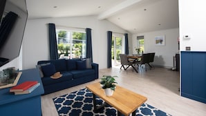 Een moderne woonkamer met een blauwe bank, een houten salontafel, en een eethoek met een tafel en stoelen.